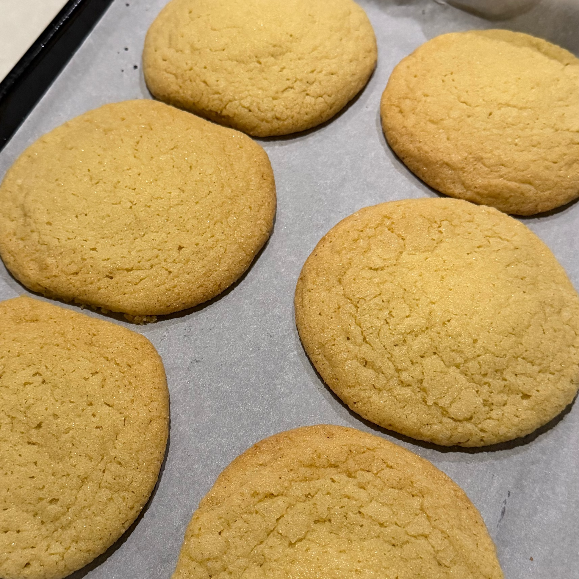 Six freshly baked cookies on a baking tray lined with parchment paper.